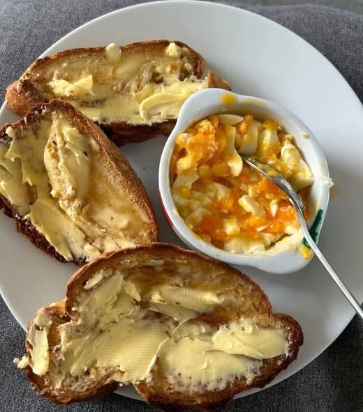 Loads of butter on tiger toast with mashed egg in a cup
